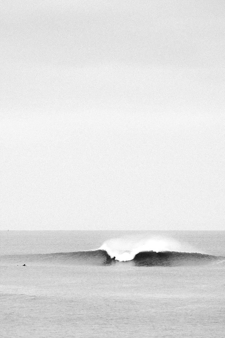 Black and white photo of a surfer paddling towards an oncoming wave.