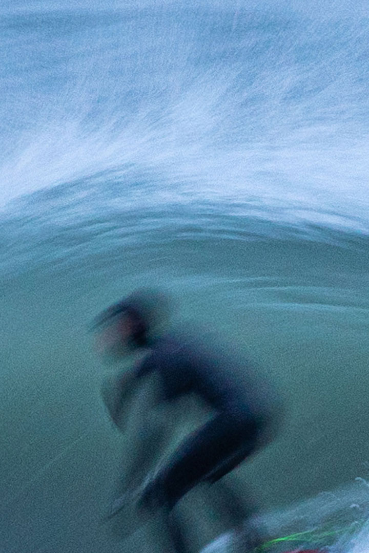 Blurred image of a surfer in a wetsuit riding under a wave.