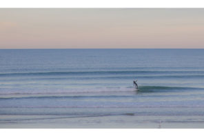 Photo of a single surfer riding a small wave with the sunrise in the background