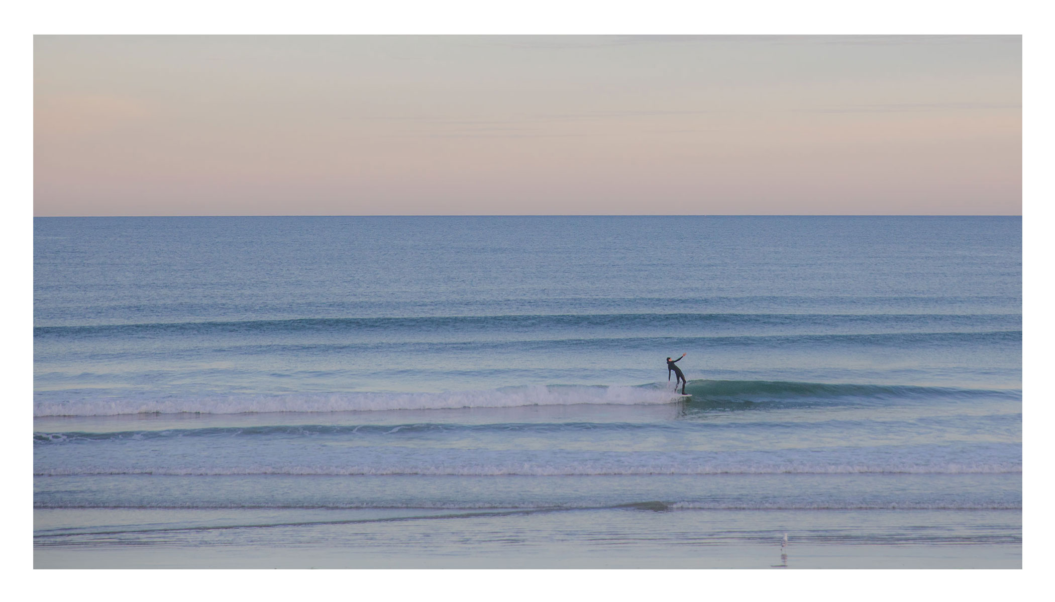 Photo of a single surfer riding a small wave with the sunrise in the background