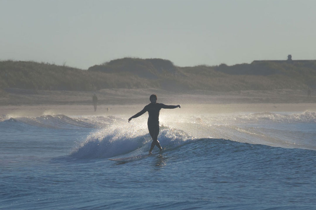 Photo of a surfer balancing on a surfboard riding a small wave as they try to walk forward on the board.