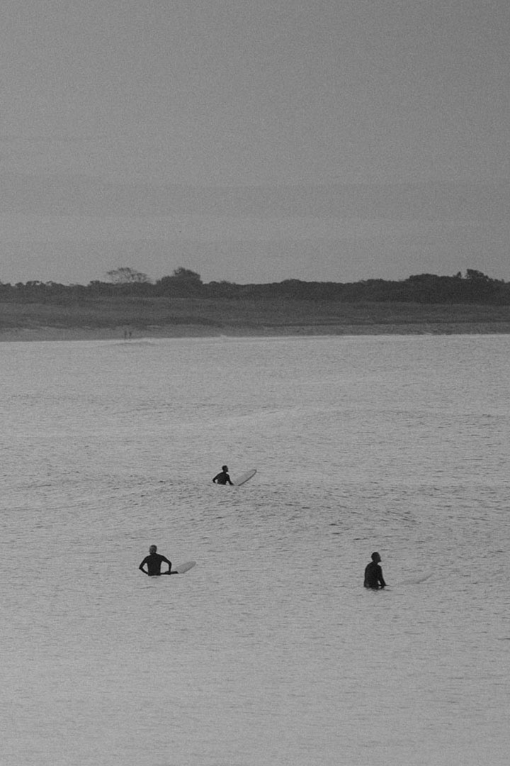 Photo of three surfers siting on their surfboards waiting for a good wave as they sit amongst small waves.