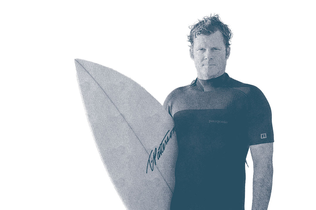 Photo of the CEO of Surfrider, Dr. Chad Nelsen, in a wetsuit holding his surfboard.