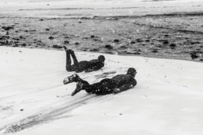 2 surfers in wetsuits sliding like seals in the snow