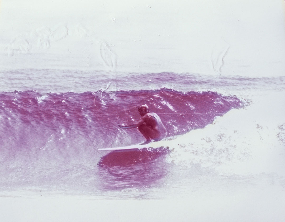 Janet MacPherson crouched down on her surfboard riding a wave.