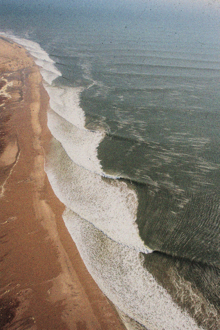 Ariel photograph of waves crashing  diagonally against a coastline.