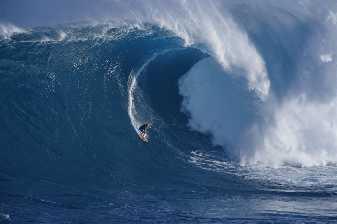 Mark Healey surfs down a large wave as the wave is about to crash over him.