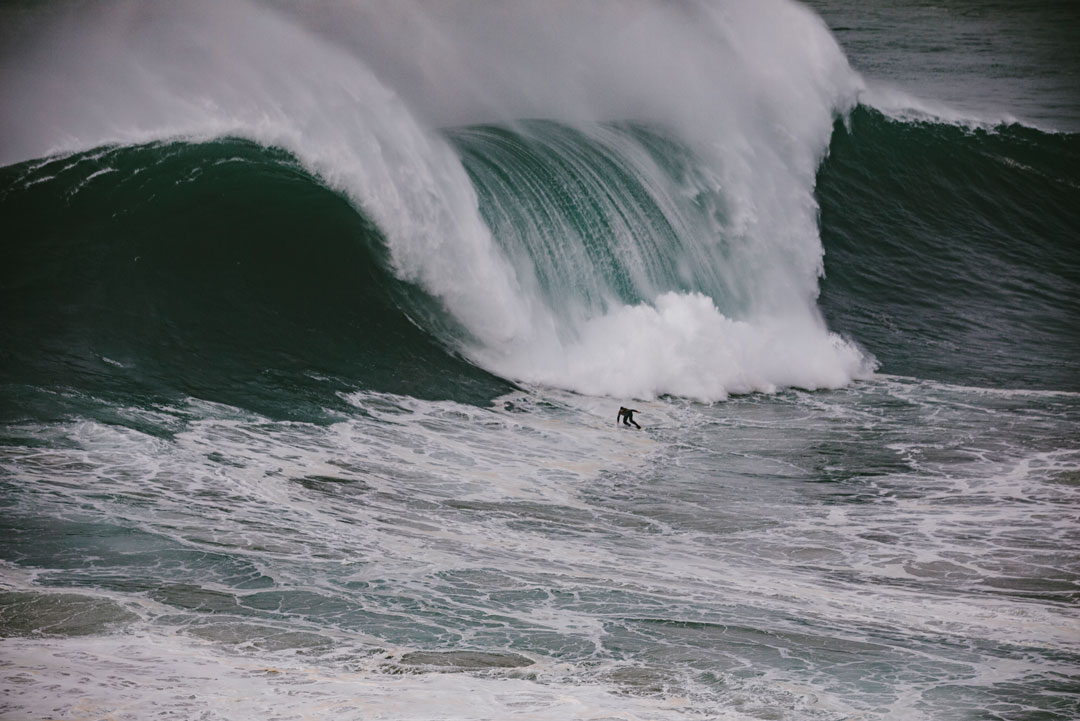 Nic Von Rupp surfing a large wave near the bottom as the white water crashes down behind him.