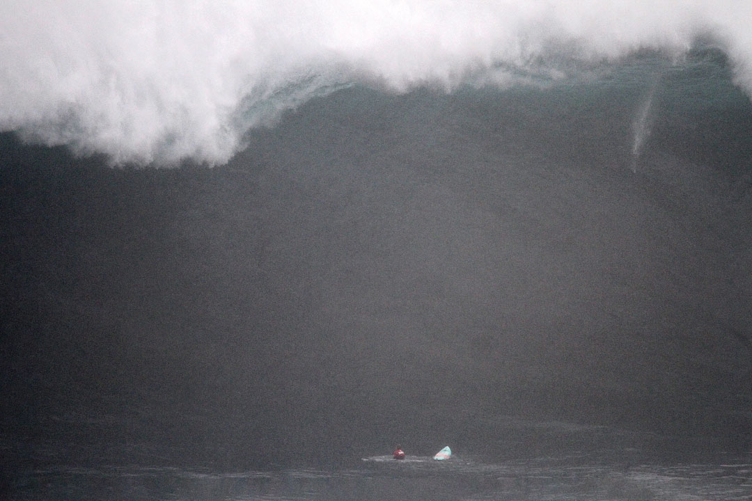 Paige Alms sitting underneath a massive dark wave as it heads over her about to crash down.