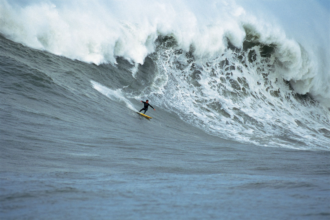 Peter Mel racing down a large wave while wearing a wetsuit.
