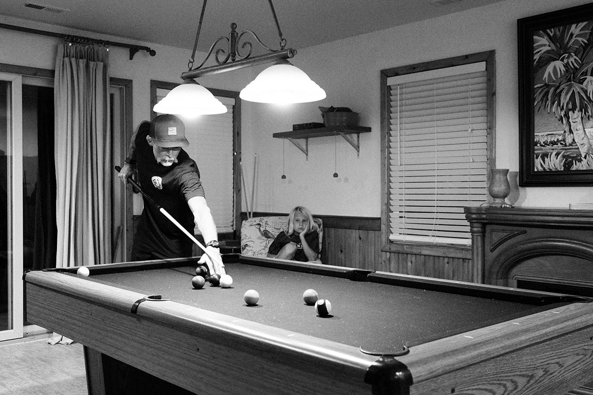 young boy watching older man play billiards