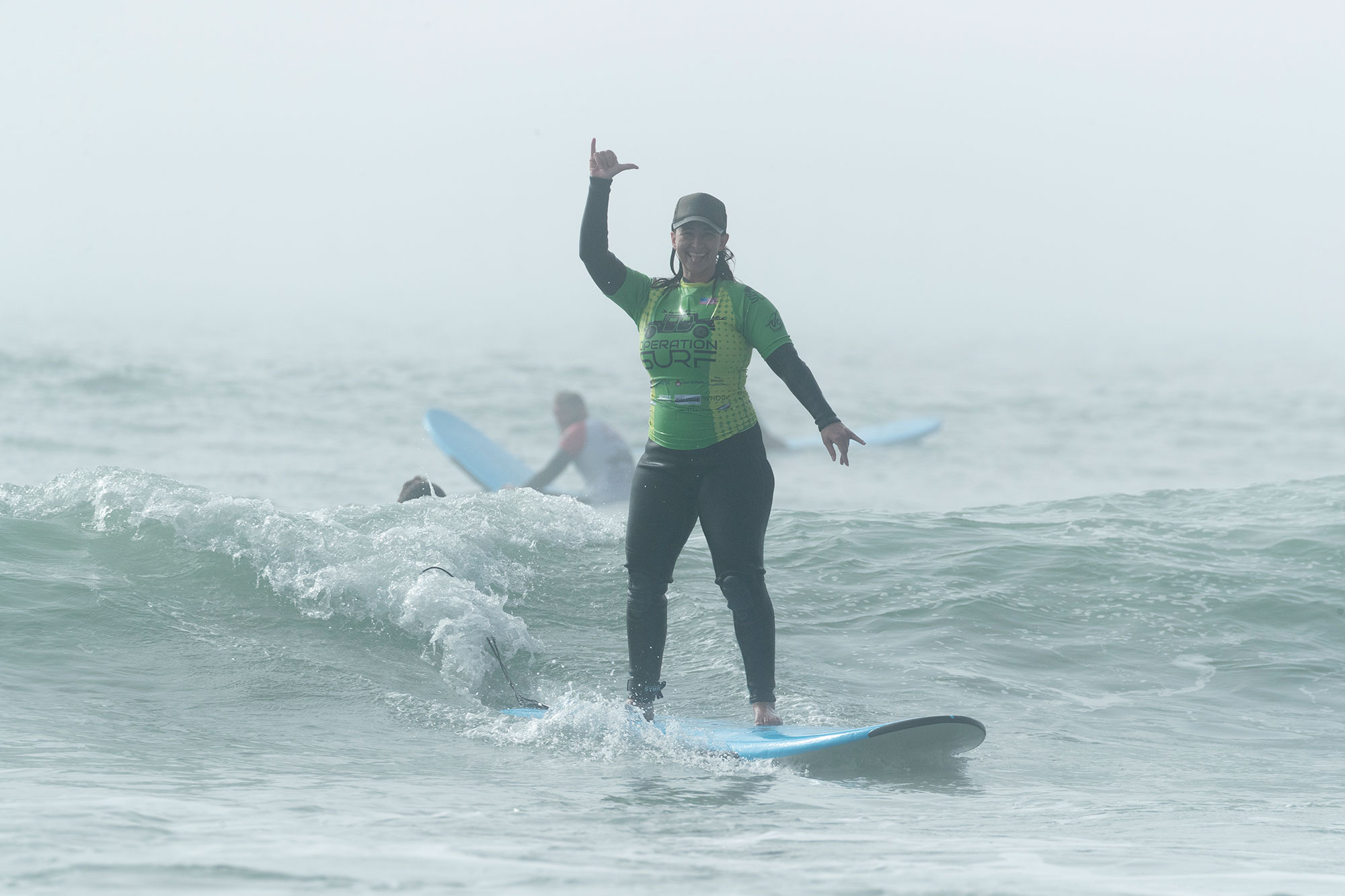 Stephanie, veteran, surfing and holding up shaka with operation surf