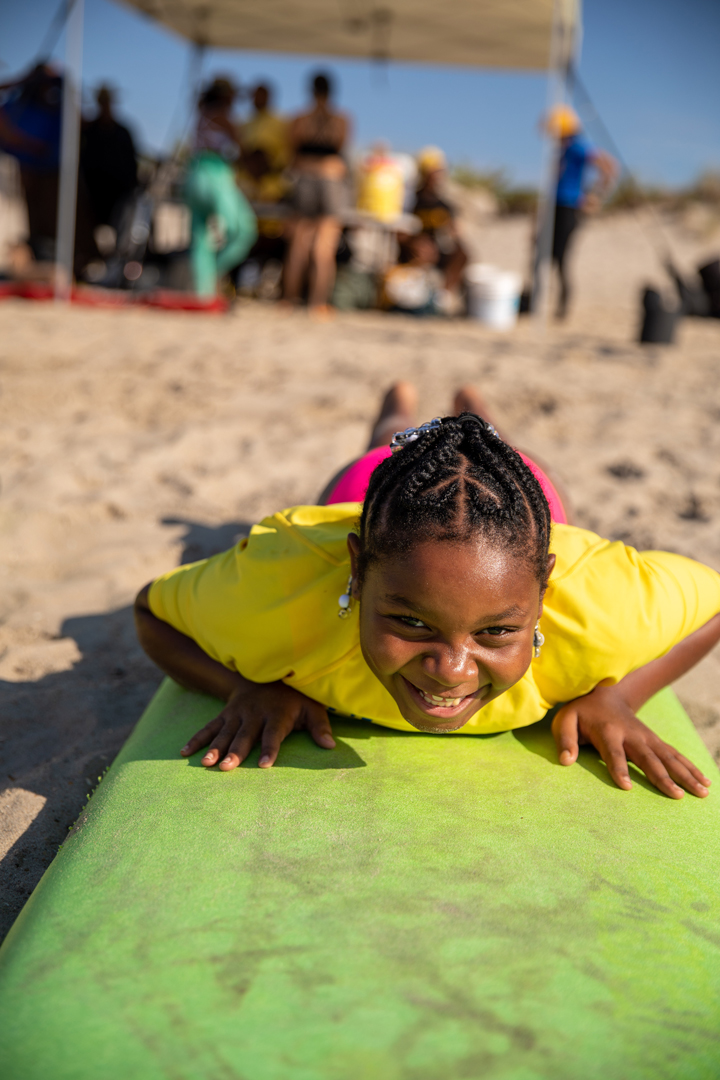 A young girl lays on her green surfboard on the beach getting ready to practice how to pop up on the board.