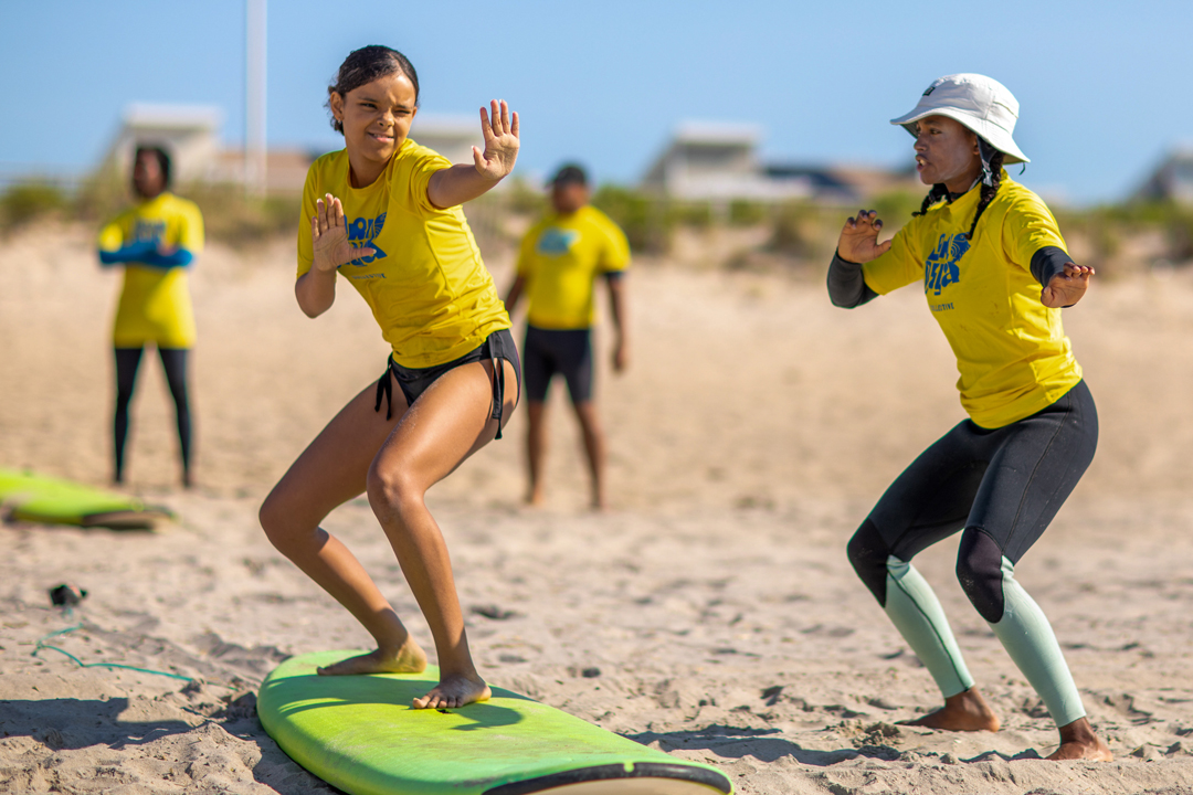 group of girls practicing their surfing form on the beach. standing on board with instructor.