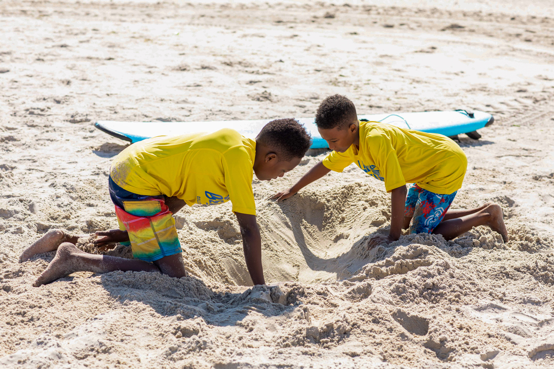 2 boys digging in the sand on the beach.