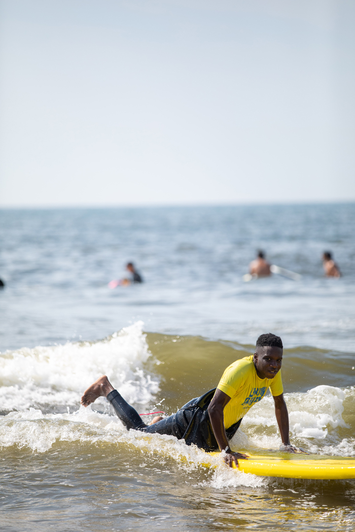 Young man in the waves pushing up on his surfboard getting ready to stand up on it.