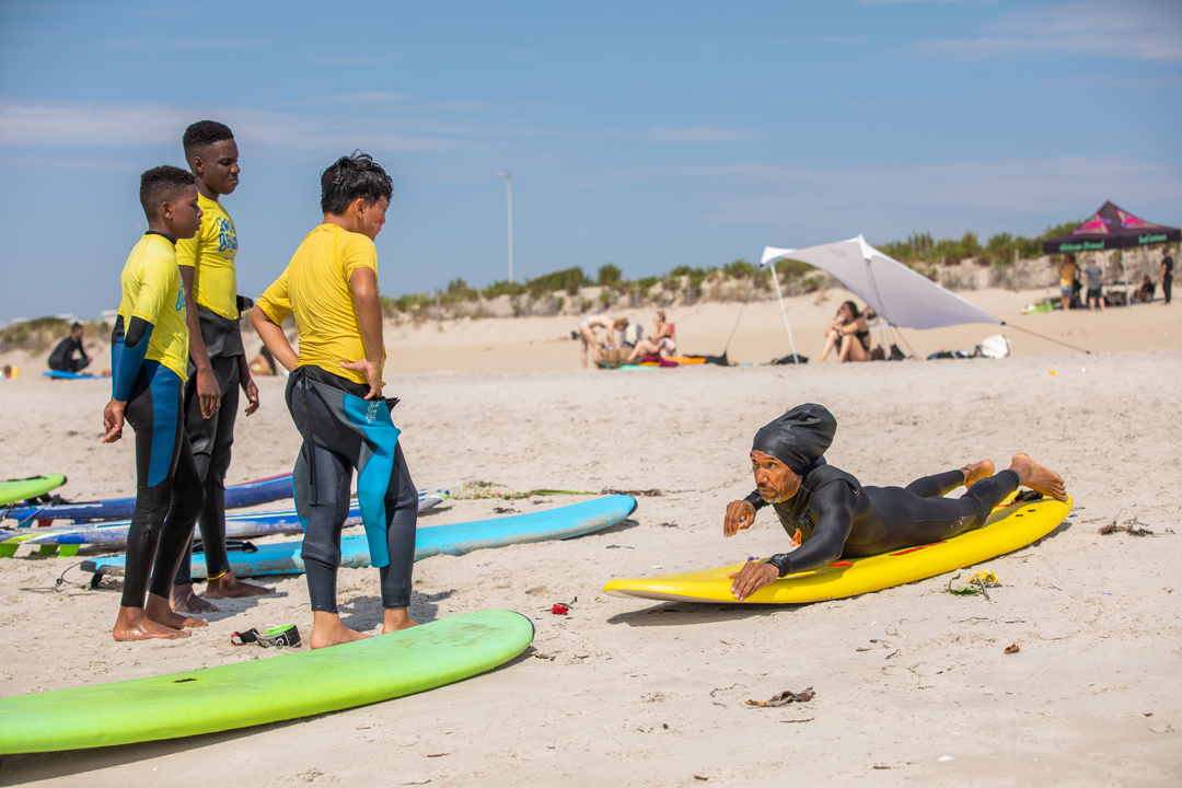 A group of kids on the beach laying on surfboard practicing how to paddle. The lay patiently on their boards watching their instructors.