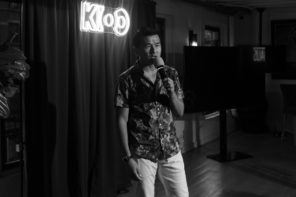 Black and white photo of Ronny Chieng performing on stage standing in front of the crowd.