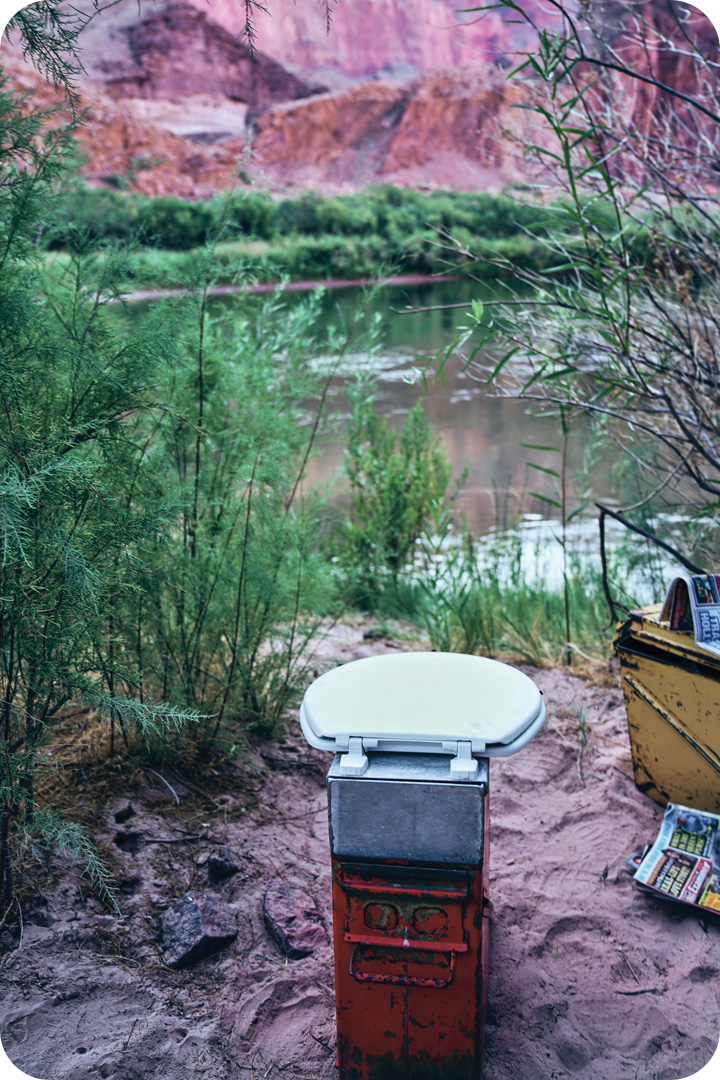 Makeshift toilet seat setting on the bank of the Colorado River. Next to it is a yellow tin box with newpapers on top of it.