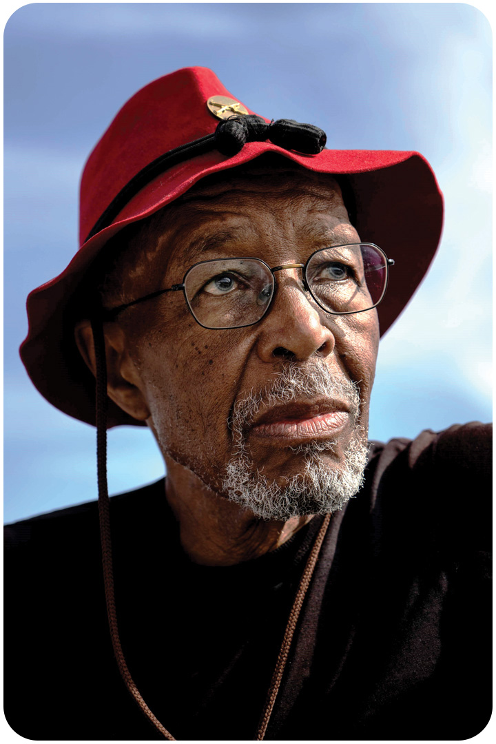 Portrait of J.R. Harris wearing his iconic red bucket hat and a pair of glasses.