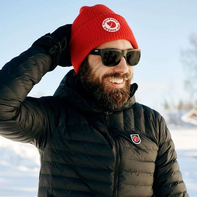 Man smiling and wearing a Fjӓllrӓven red hat beanie