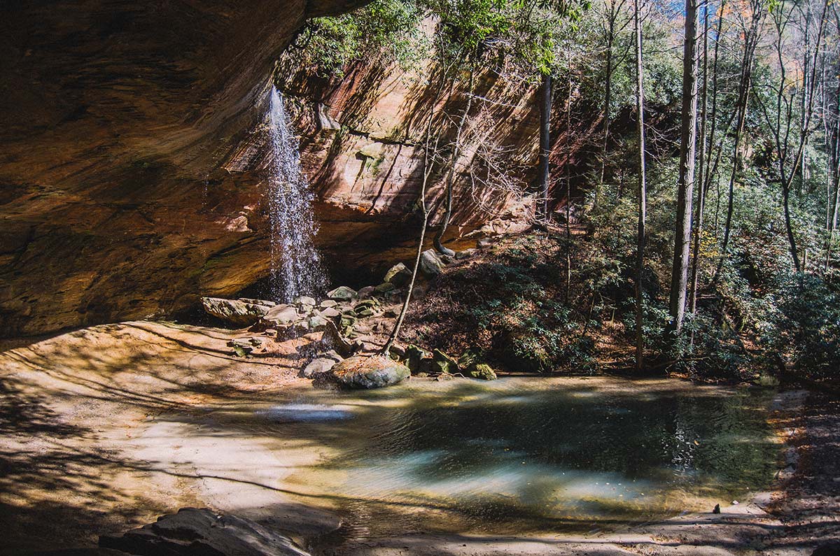 The Copperas falls in the in the Daniel Boone National Forest is a small waterfall over a large rock ledge. Below is a dark aquamarine pool of water resting under the trees. 