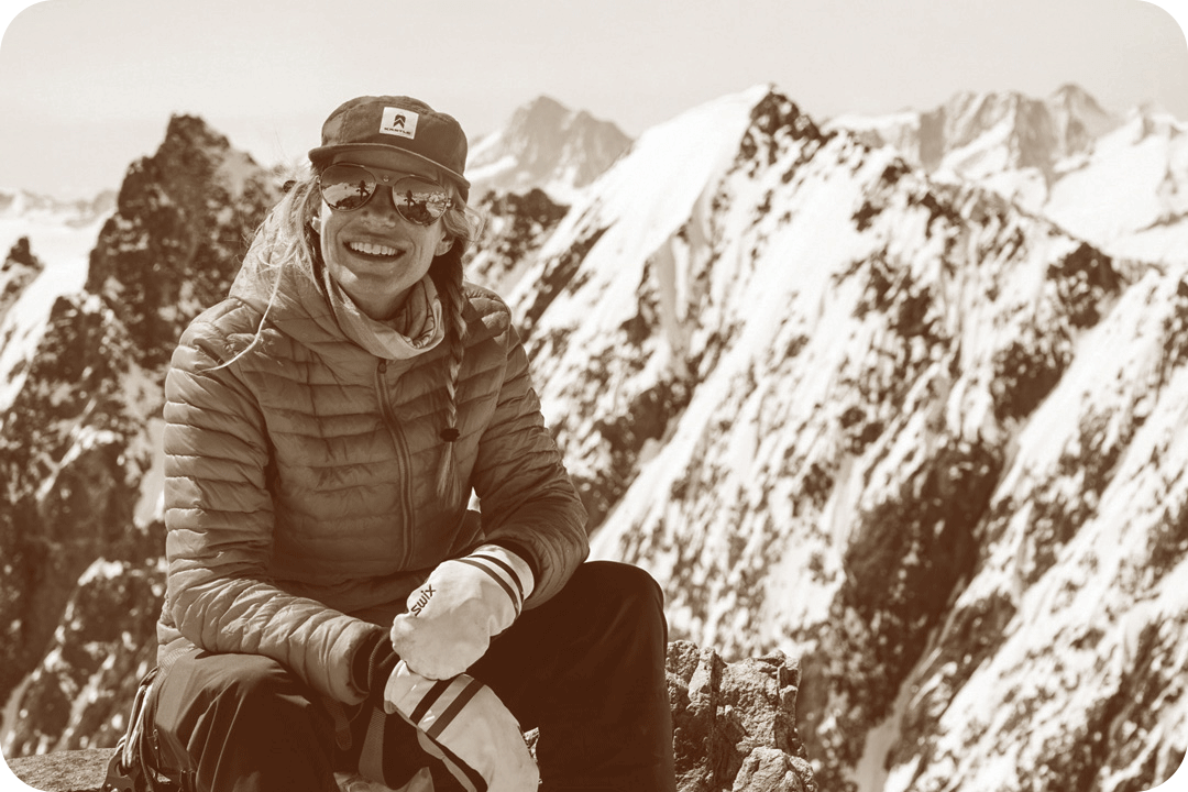 Christy Mahone, environmental advocate, smiling for a picture on a mountain. She's wearing a thin puffer jacket, gloves, sunglasses, and a flat-bill baseball hat.