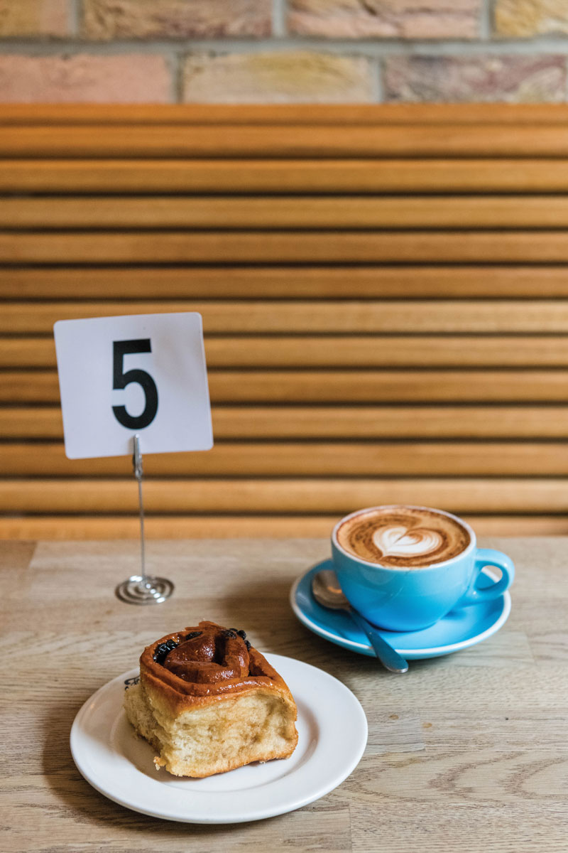 Table number 5 card with a cinnamon roll and a latte in a blue mug on a wood table. 