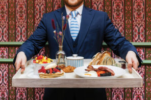 Man in a suit holding a plate of breakfast.