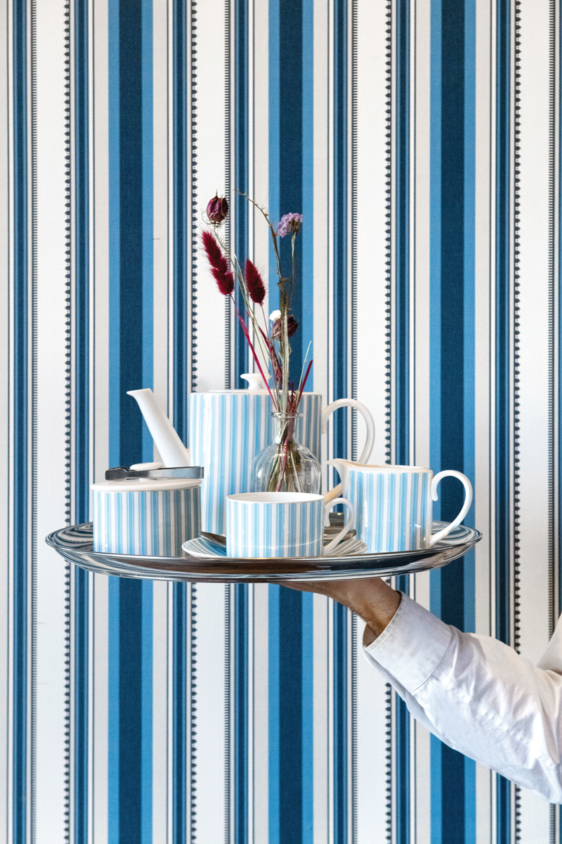 Striped wallpaper and tea set being held up on a silver tray