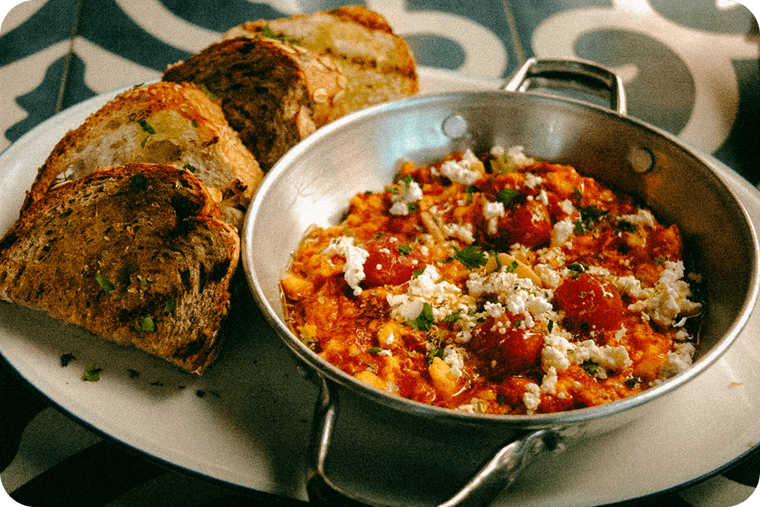 Metal bowl of eggs scrambled with feta cheese and tomatoes. Four slices of toast sit on the plate next to the bowl.