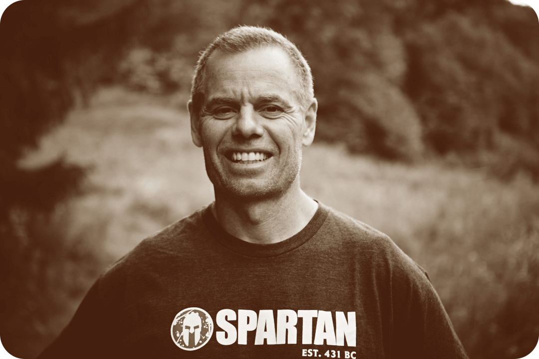 Joe De Sena, Spartan Race Founder, smiling for a picture outside while wearing a Spartan Race shirt.