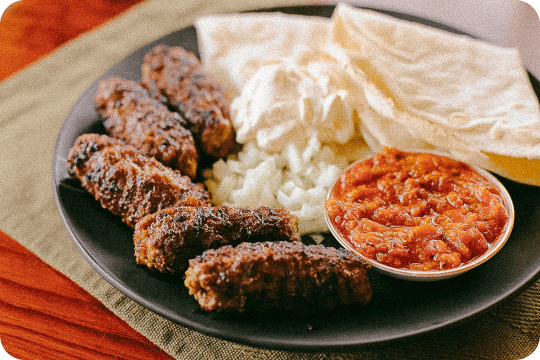 A plate of five mini sausages, chopped onions, a small bowl of red sauce, and a type of folded bread.