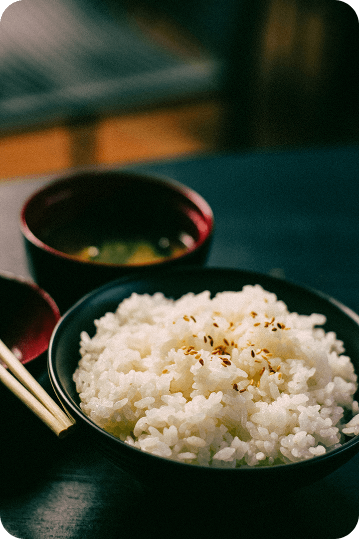 One bowl of rice with seeds on top and another of clear soup. A pair of chopsticks sit next to the bowls.