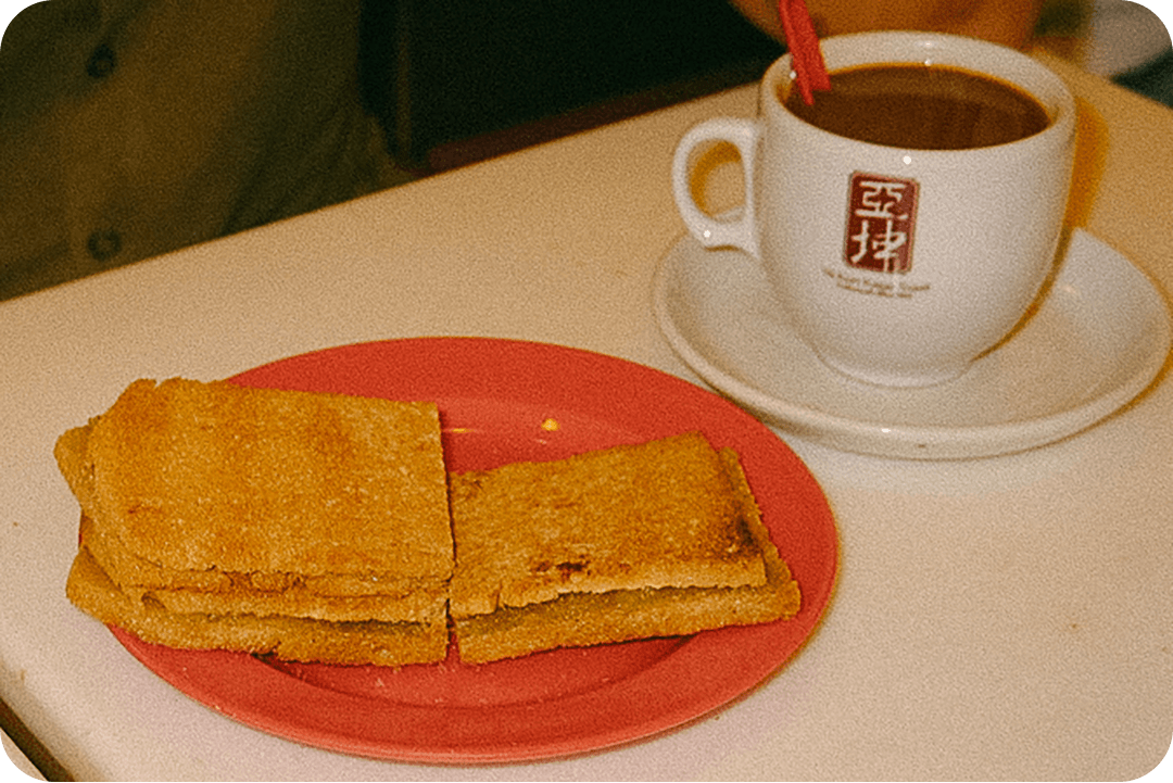 Kaya toast sandwich sitting on a read plate. A cup of coffee is sitting on the table behind the toast.