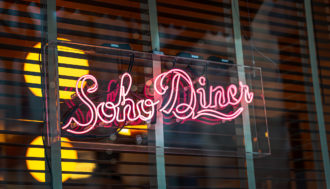 Pink neon sign reading "Soho Diner" on the outside of a window