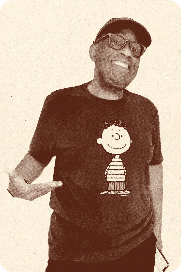 Al Roker, from the Today show, smiling for a picture. He's wearing thick framed glasses, a hat, and a t-shirt with a Charlie Brown character on it.