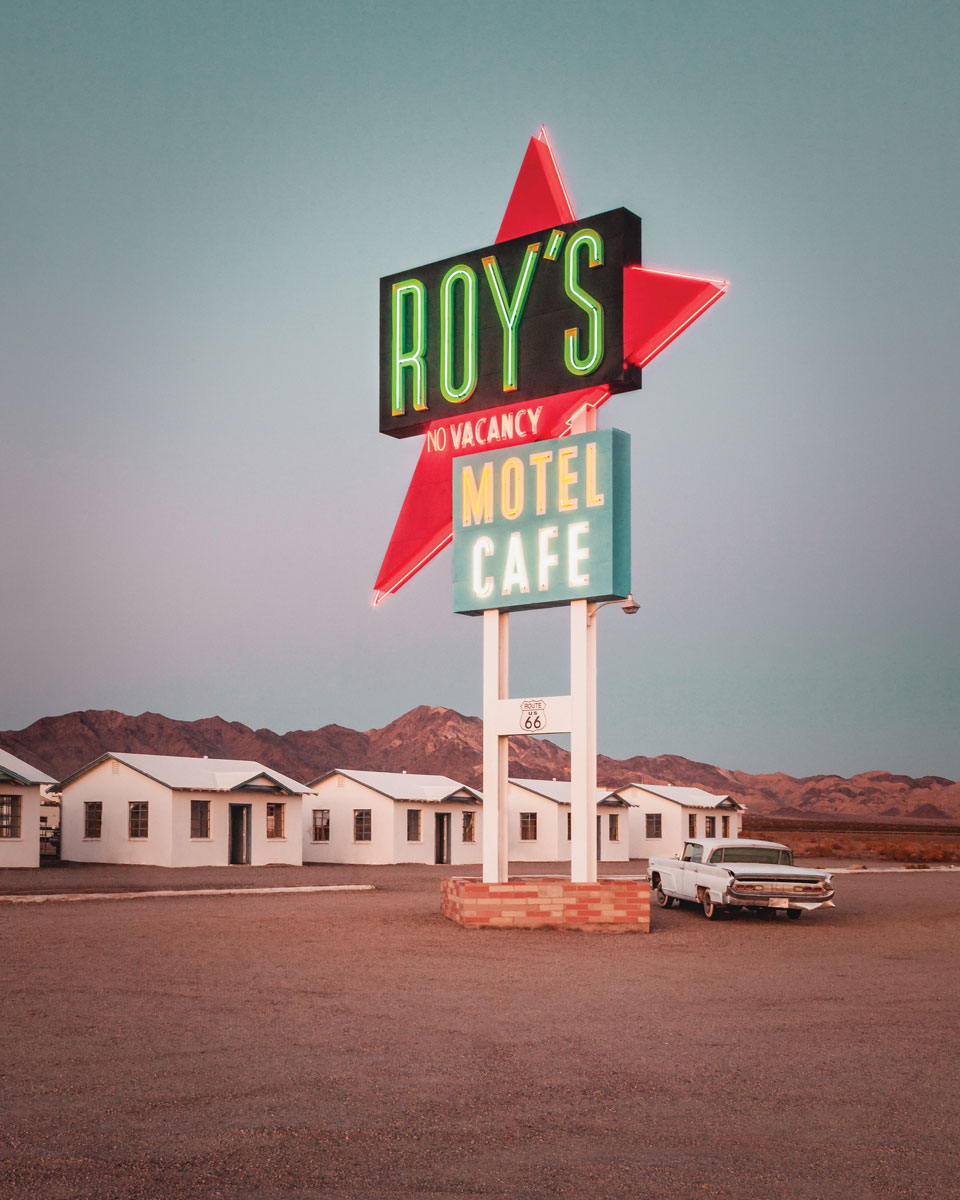 Roy's motel cafe neon sign with classic car parked next to it.