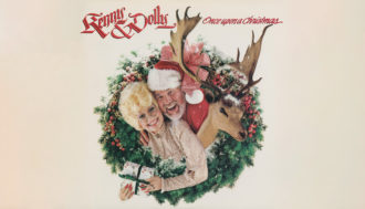 Dolly Parton and Kenny Roger's christmas album cover, "Once upon a Christmas" that has Parton and Rogers with their heads stick through a wreath with a reindeer.