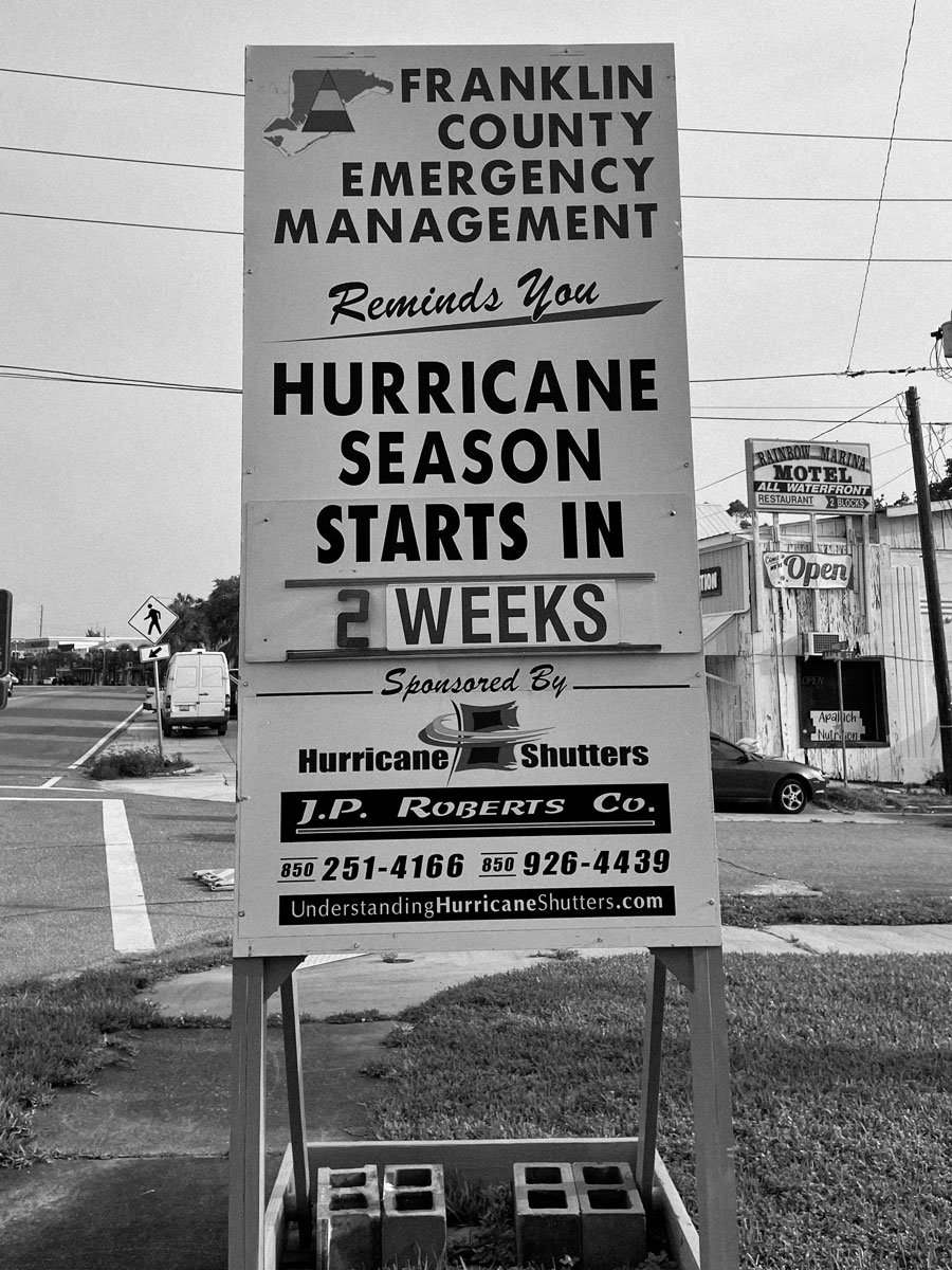 Black and white photo of an old-fashioned vertical sign on the side of a road announcing the approach of hurricane season.