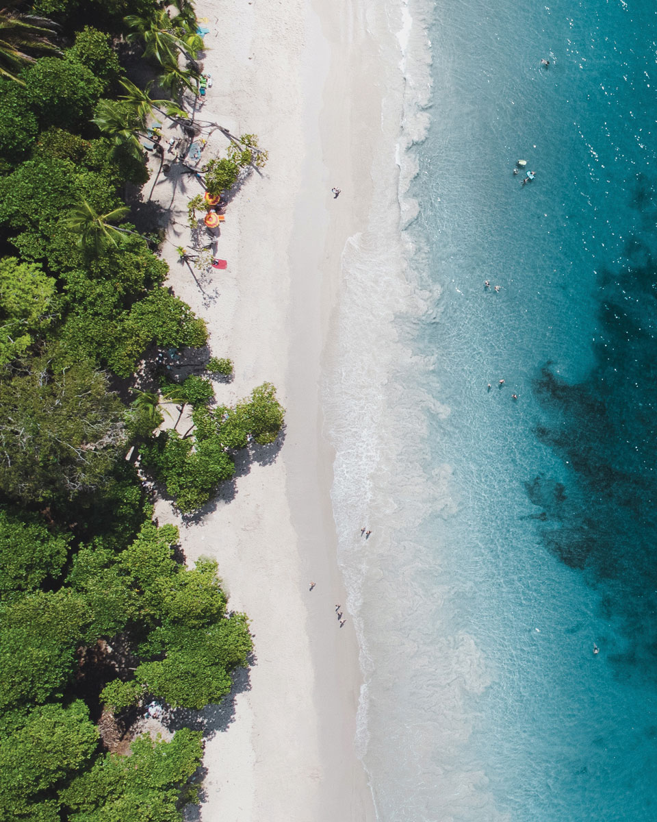 Overhead shot of a beach with jungle on one side and blue water on the other.