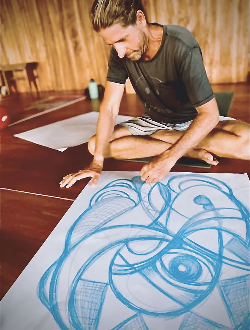 Alex Lanau painting blue swirls and abstract forms on a white canvas sitting on the ground.