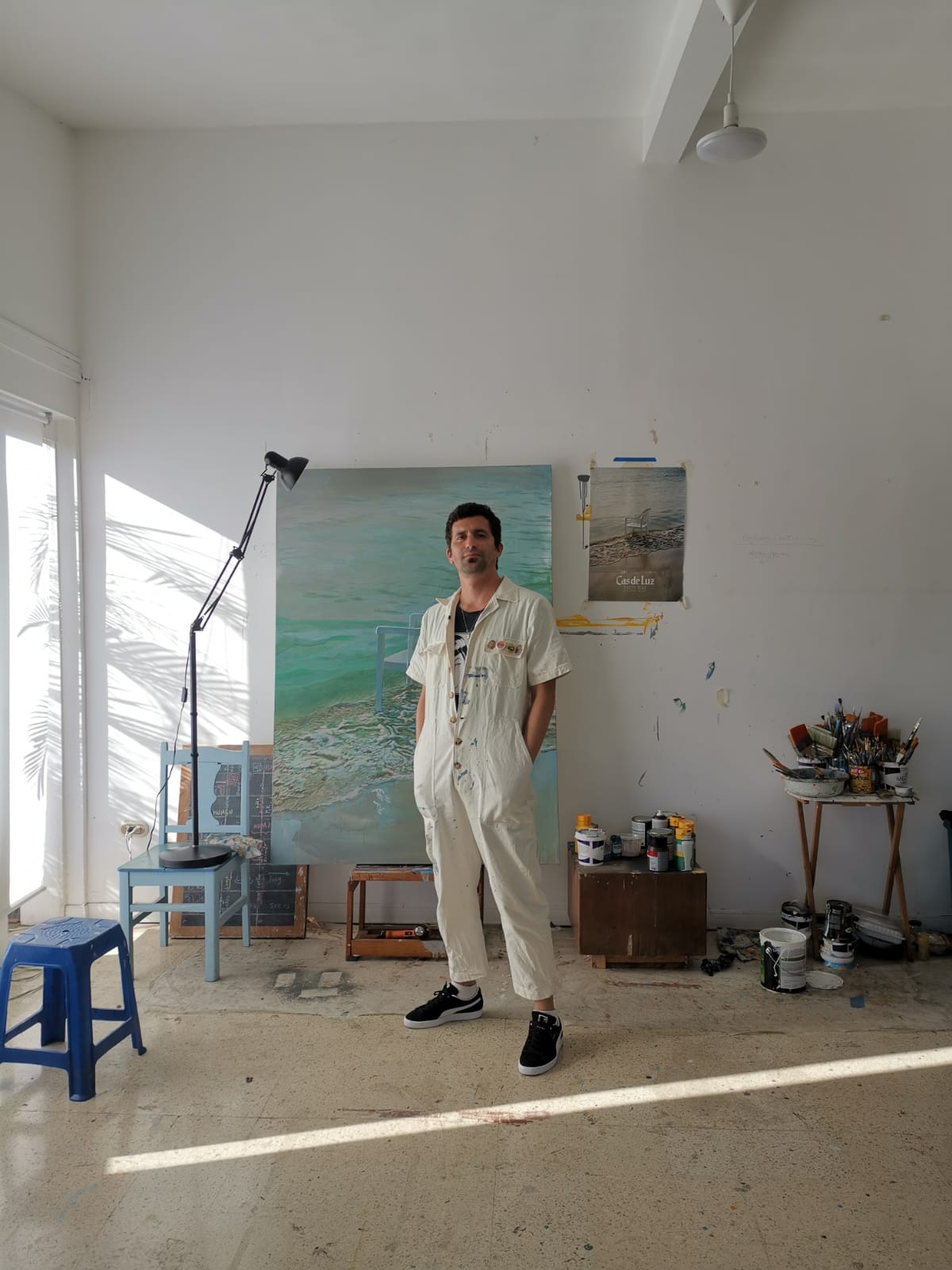 Fabian Monge standing in studio in front of a large painting of the beach