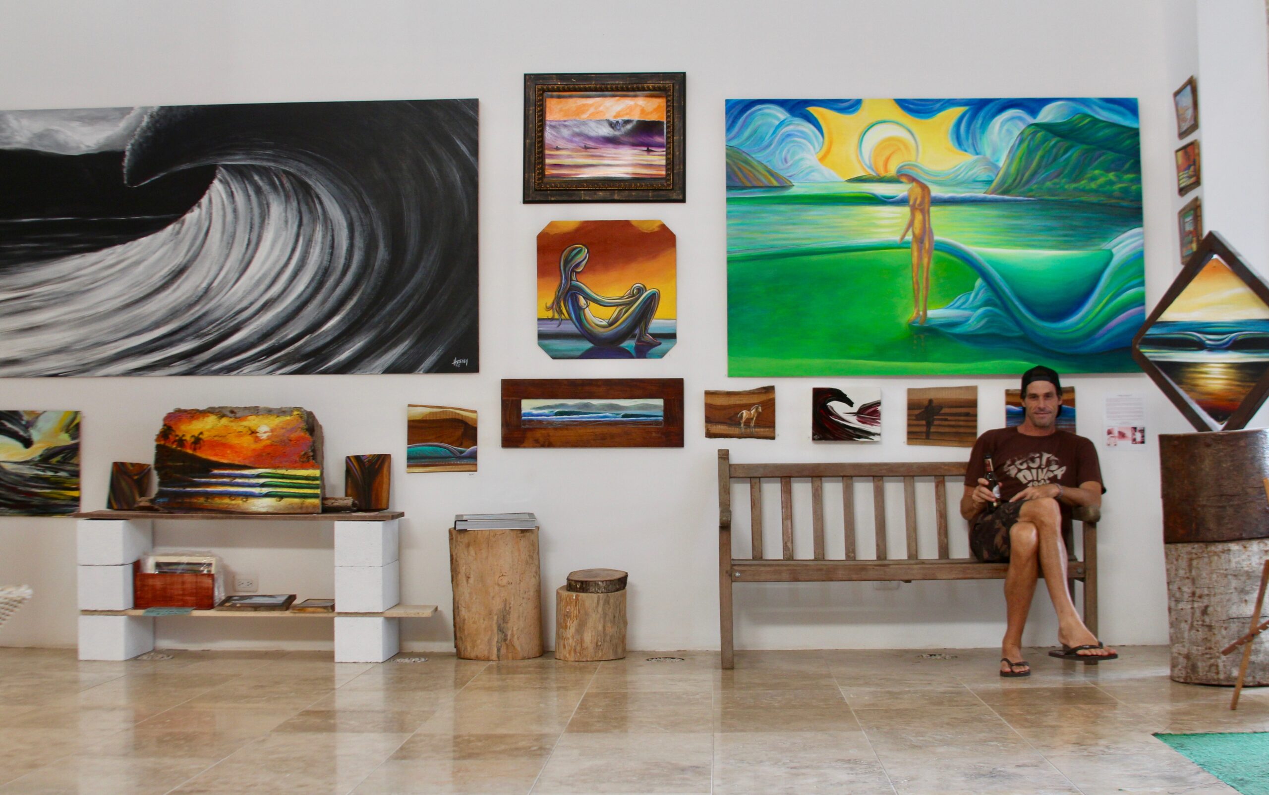 Robb Havassy sitting on a bench in front of his gallery of vibrant paintings.