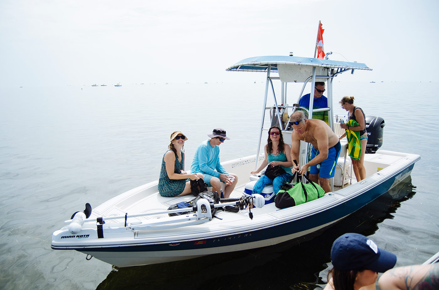 A day along the Gulf Coast with Rabbit Hole. Several people sit and or stand in a small boat, floating in the gulf of Mexico. The background is hazy. 