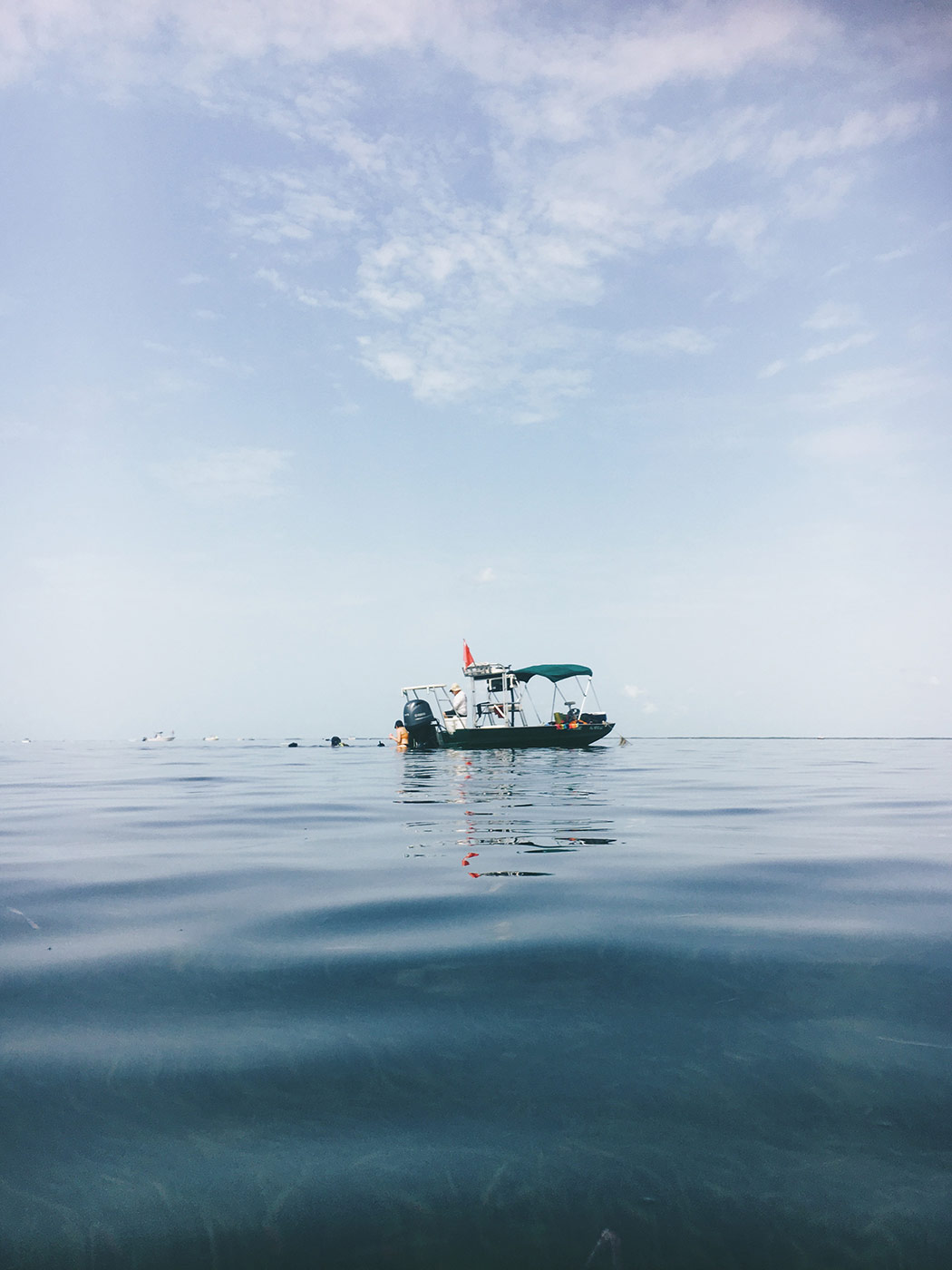 A day along the Gulf Coast with Rabbit Hole. A small boat sits on still blue water. Blue hazy sky is in the background.