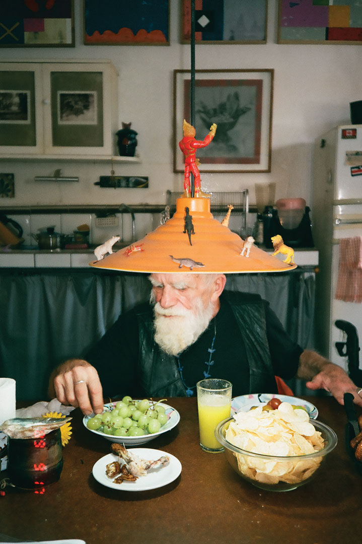 Gerardo Ramirez Castro wearing a lampshade with toy figurines glued to it sitting at a table enjoying some snacks. 