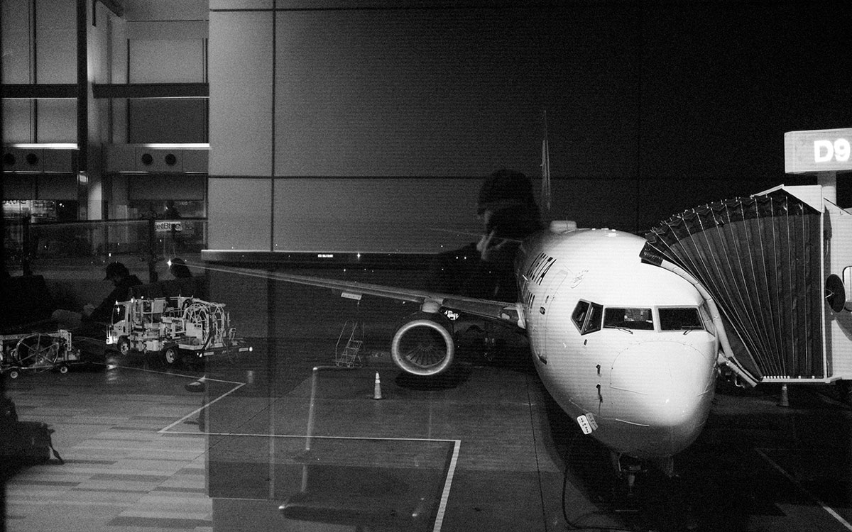 Black and white photo of a white airplane connected to the skyway ramp in an airplane hangar.