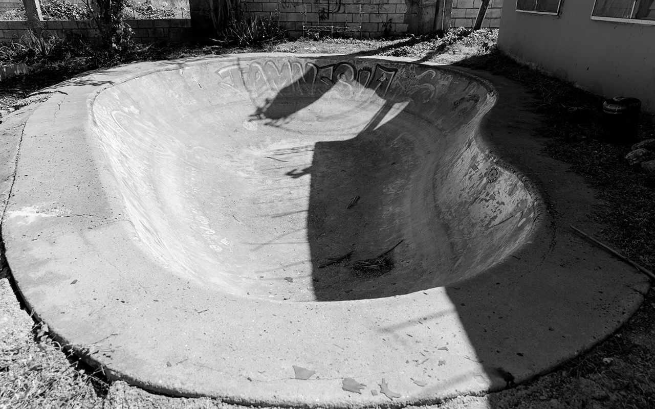Photo of an empty lagoon shape cement swimming pool with graffiti inside it. The pool is used for skating.