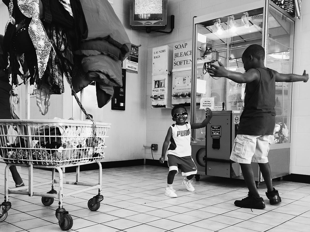 Black and white photo of two boys (one an infant, one a toddler) dancing together and playing in a laundromat.
